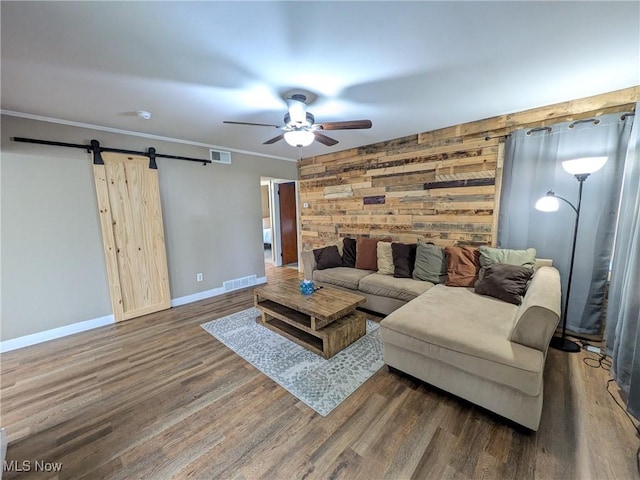 living area featuring a ceiling fan, a barn door, wooden walls, baseboards, and wood finished floors