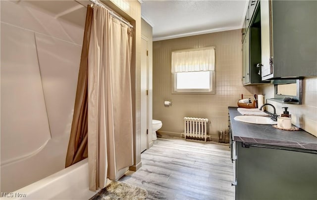 bathroom with radiator, toilet, wood finished floors, tile walls, and vanity