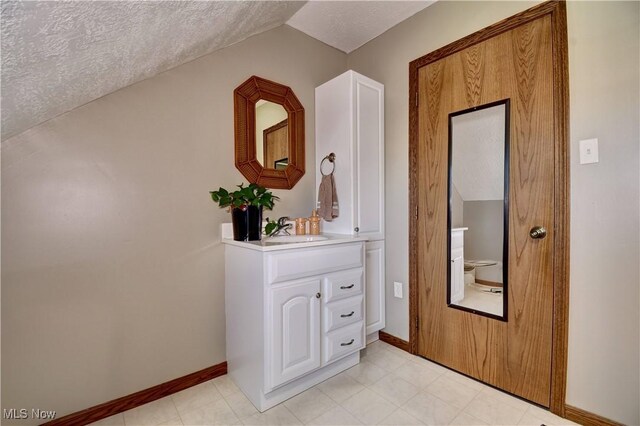 hall with a sink, baseboards, a textured ceiling, and vaulted ceiling