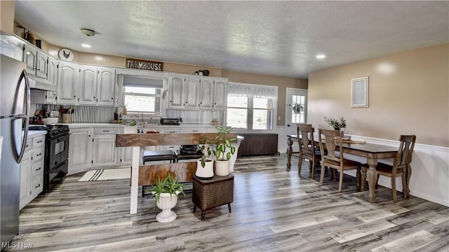 kitchen with black gas range oven, freestanding refrigerator, under cabinet range hood, light wood-type flooring, and a textured ceiling