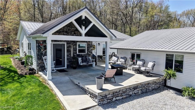 rear view of property with a patio, metal roof, a standing seam roof, stone siding, and a lawn