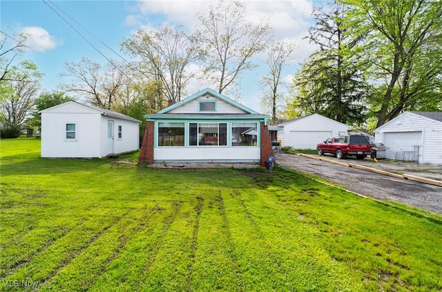 back of house with a detached garage, a lawn, and an outbuilding