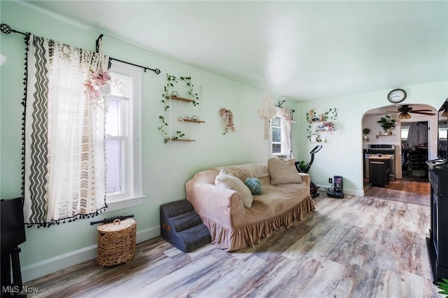 living area featuring wood finished floors, arched walkways, ceiling fan, and baseboards