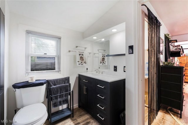bathroom with wood finished floors, toilet, vanity, baseboards, and recessed lighting