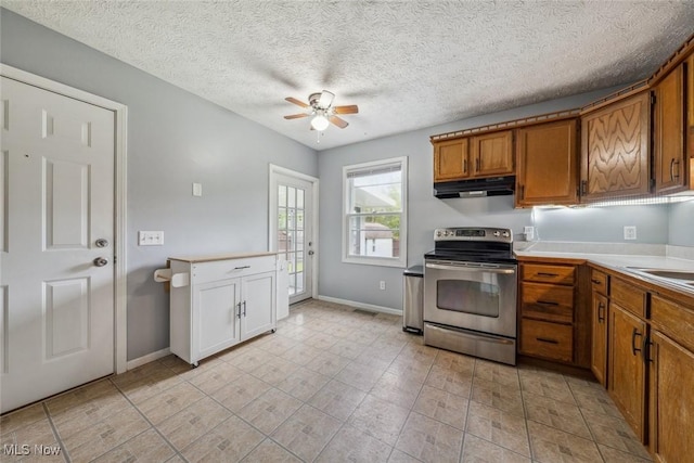 kitchen with stainless steel electric range oven, brown cabinetry, under cabinet range hood, ceiling fan, and baseboards