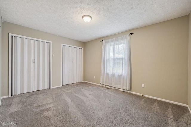 unfurnished bedroom featuring two closets, carpet, baseboards, and a textured ceiling