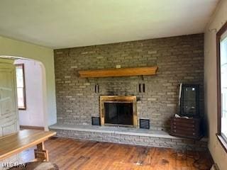 unfurnished living room with a brick fireplace, wood finished floors, and arched walkways