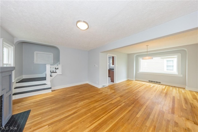 unfurnished living room featuring light wood-type flooring, a fireplace with flush hearth, a textured ceiling, stairs, and baseboards