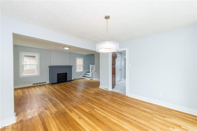unfurnished living room featuring light wood-style floors, a fireplace with flush hearth, baseboards, and stairway