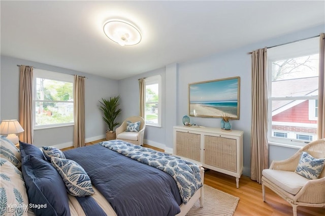 bedroom featuring multiple windows, light wood-style floors, and baseboards