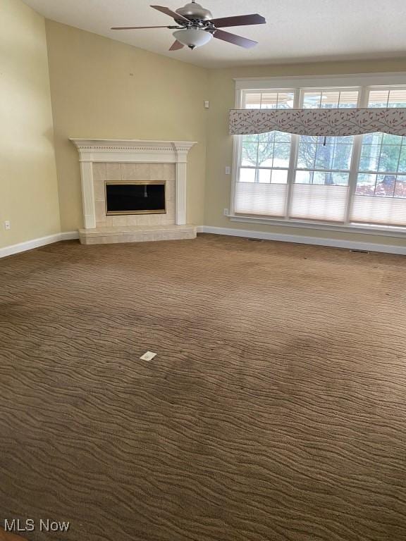 unfurnished living room featuring baseboards, a ceiling fan, a tile fireplace, and dark colored carpet