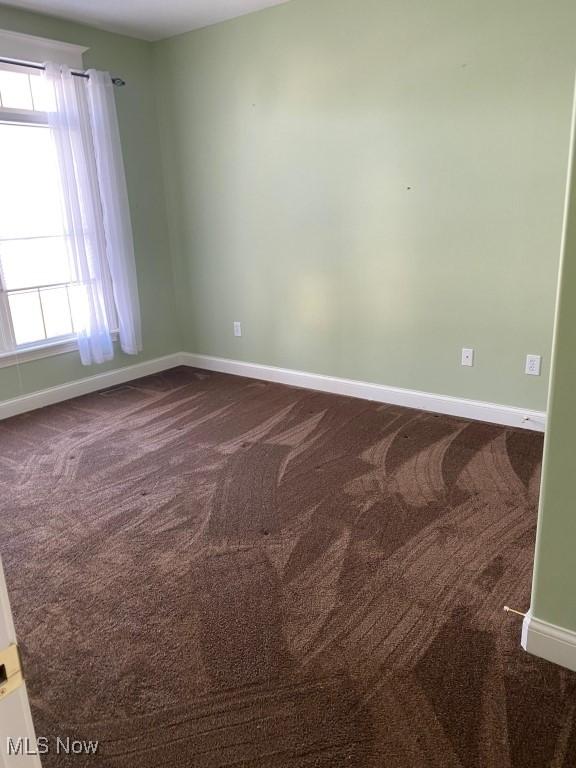 spare room featuring dark carpet and baseboards