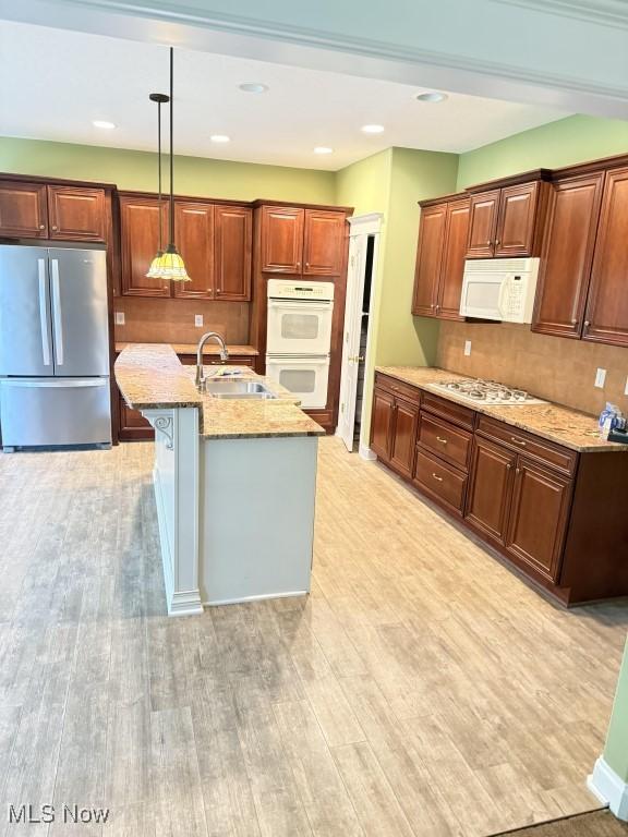 kitchen with white appliances, a sink, light wood finished floors, light stone countertops, and decorative light fixtures