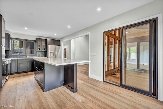 kitchen featuring stainless steel fridge with ice dispenser, light countertops, a center island, light wood-style flooring, and plenty of natural light