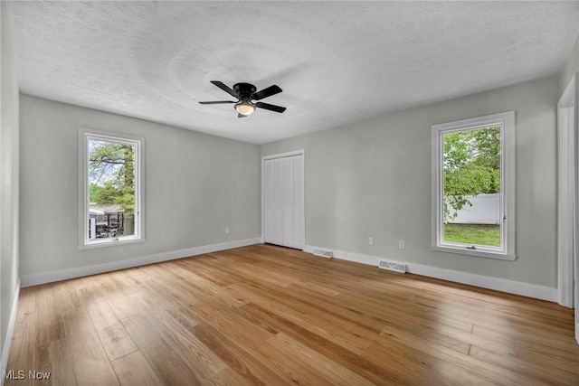 empty room with healthy amount of natural light, wood finished floors, baseboards, ceiling fan, and a textured ceiling
