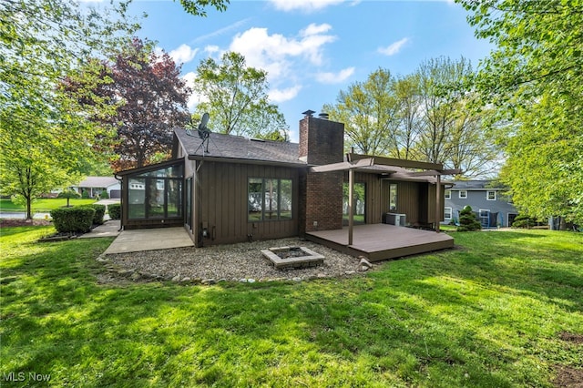 rear view of house with board and batten siding, a chimney, a wooden deck, a yard, and central AC