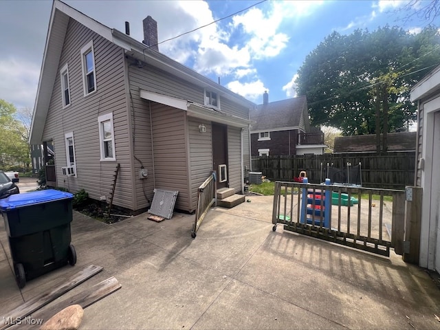 back of house with entry steps, fence, a chimney, and a patio