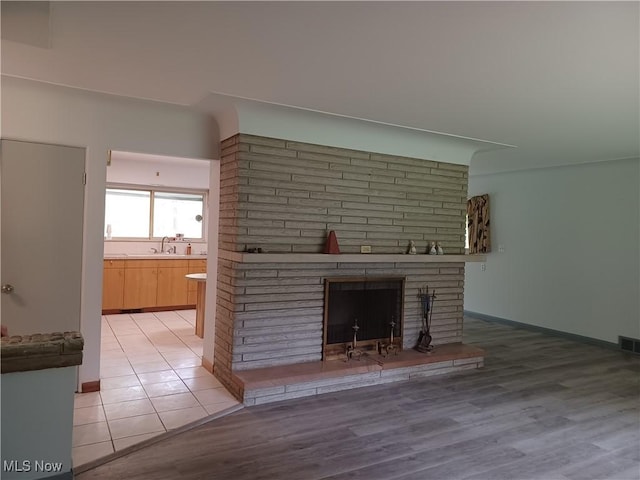 1050 Park Cir, Girard, OH 44420 - unfurnished living room featuring a brick fireplace, a sink, light wood-style floors, and baseboards