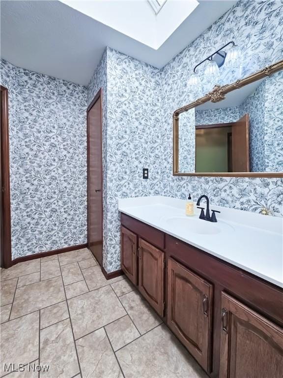 bathroom with a skylight, wallpapered walls, vanity, and tile patterned flooring