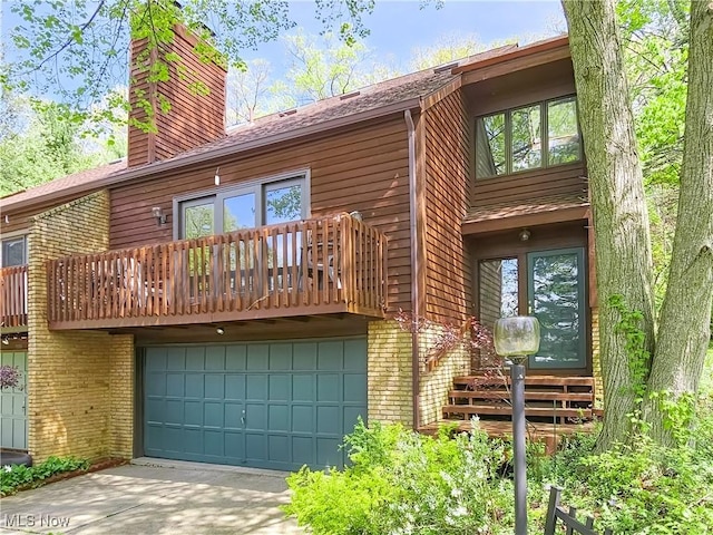 back of house featuring an attached garage, a chimney, driveway, and brick siding