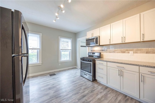 kitchen with stainless steel appliances, backsplash, white cabinetry, and light stone countertops