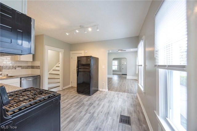 kitchen featuring freestanding refrigerator, range with gas cooktop, dishwasher, arched walkways, and baseboards