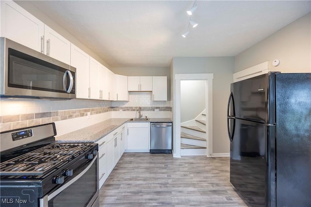 kitchen with stainless steel appliances, white cabinetry, tasteful backsplash, and light wood-style floors
