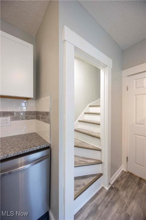 staircase featuring a textured ceiling, wood finished floors, and baseboards