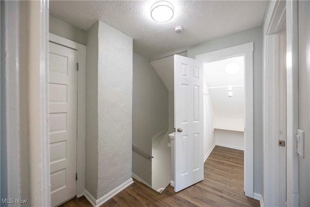 corridor with an upstairs landing, wood finished floors, baseboards, and a textured ceiling