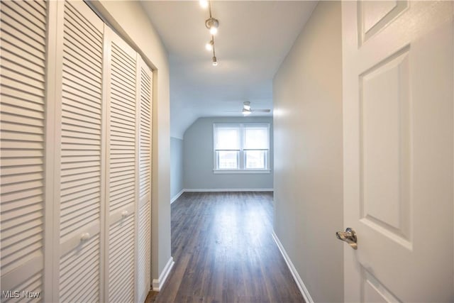 corridor featuring baseboards, dark wood-type flooring, and vaulted ceiling