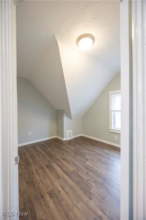 additional living space featuring vaulted ceiling, dark wood finished floors, a textured ceiling, and baseboards