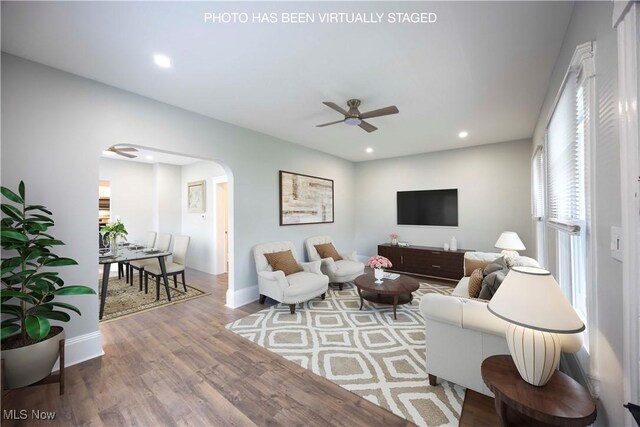 living area featuring arched walkways, a ceiling fan, wood finished floors, baseboards, and recessed lighting