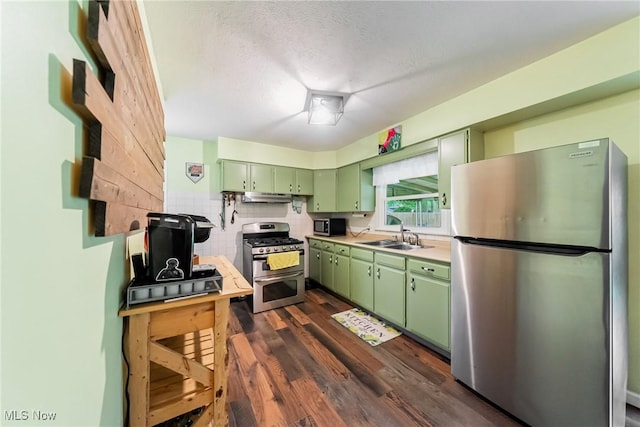 kitchen with green cabinetry, stainless steel appliances, a sink, under cabinet range hood, and light countertops