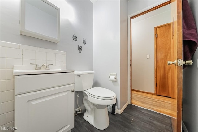 half bathroom featuring wood finished floors, vanity, toilet, and baseboards