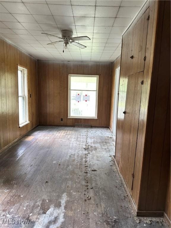 empty room featuring hardwood / wood-style flooring, a ceiling fan, wood walls, and baseboards