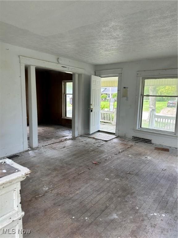 unfurnished living room featuring wood-type flooring, plenty of natural light, and a textured ceiling