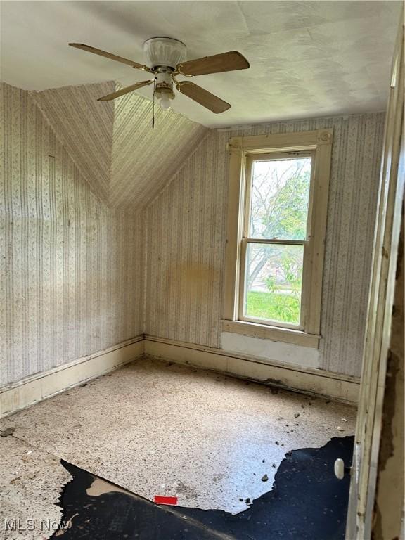 bonus room with ceiling fan and wallpapered walls