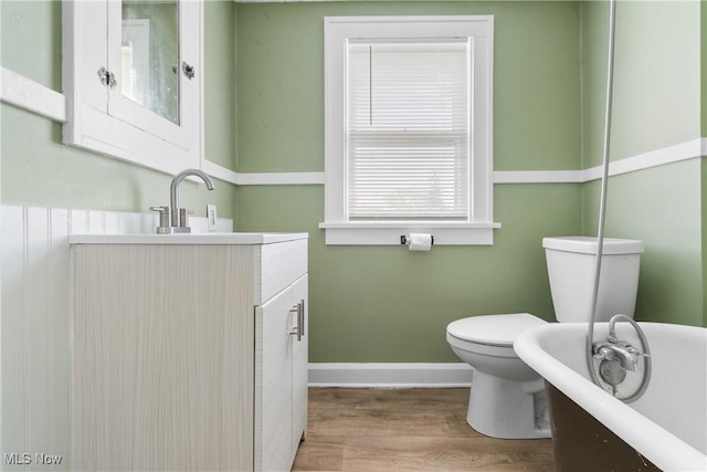 full bathroom featuring toilet, a freestanding bath, wood finished floors, vanity, and baseboards