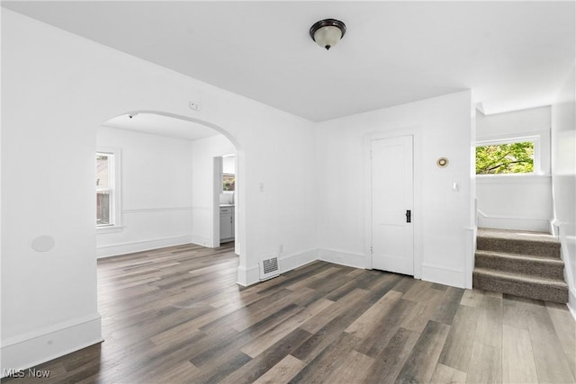 empty room with arched walkways, dark wood-style flooring, stairway, and baseboards