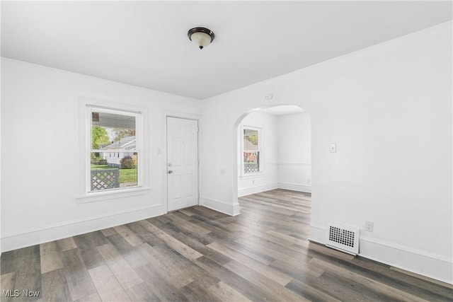 unfurnished room with arched walkways, wood finished floors, and baseboards