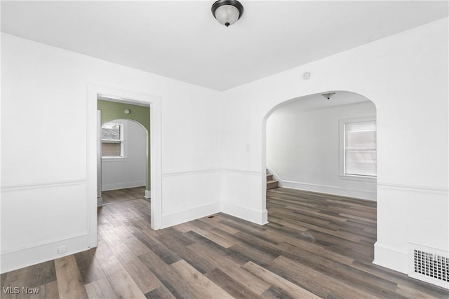 empty room with arched walkways, wood finished floors, stairway, and baseboards