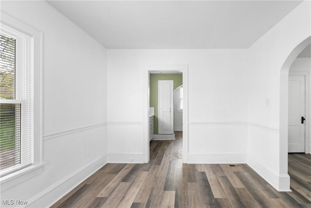 unfurnished room featuring arched walkways, dark wood-type flooring, and baseboards