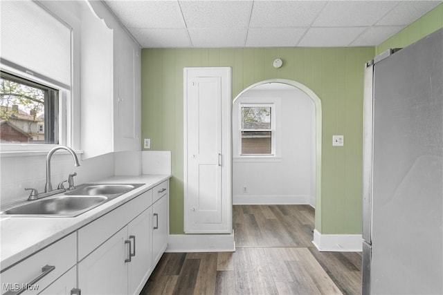 kitchen featuring a sink, white cabinets, dark wood finished floors, light countertops, and a paneled ceiling