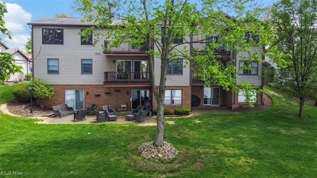 rear view of house featuring a balcony, a patio, a lawn, and brick siding
