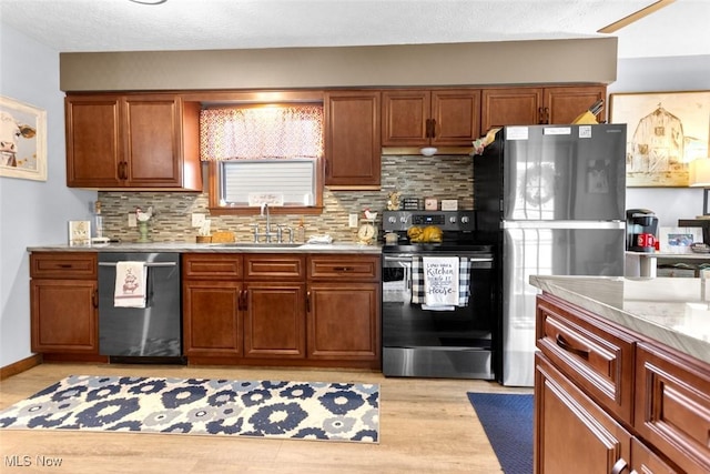 kitchen featuring stainless steel appliances, a sink, backsplash, light countertops, and light wood-type flooring