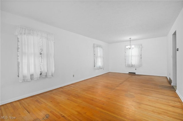 unfurnished room featuring a chandelier, light wood-style floors, and baseboards