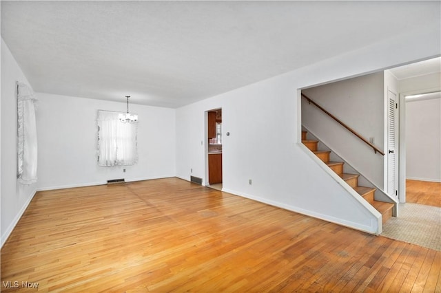 unfurnished living room with light wood finished floors, a chandelier, stairway, and baseboards