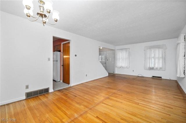 unfurnished living room featuring a chandelier, wood-type flooring, and baseboards