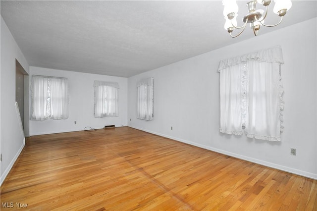 spare room featuring a chandelier, light wood-style floors, and baseboards