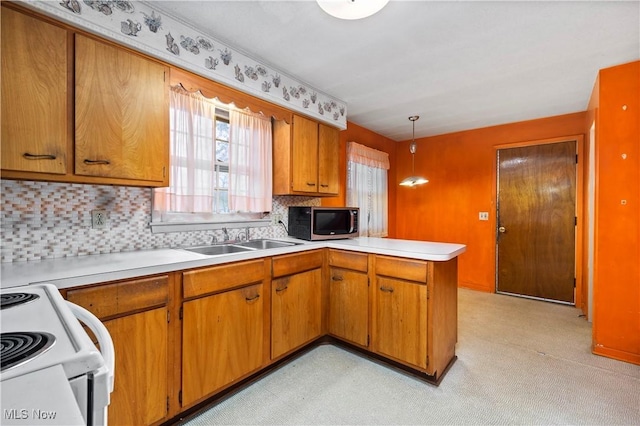 kitchen with stainless steel microwave, a sink, a peninsula, light countertops, and brown cabinets